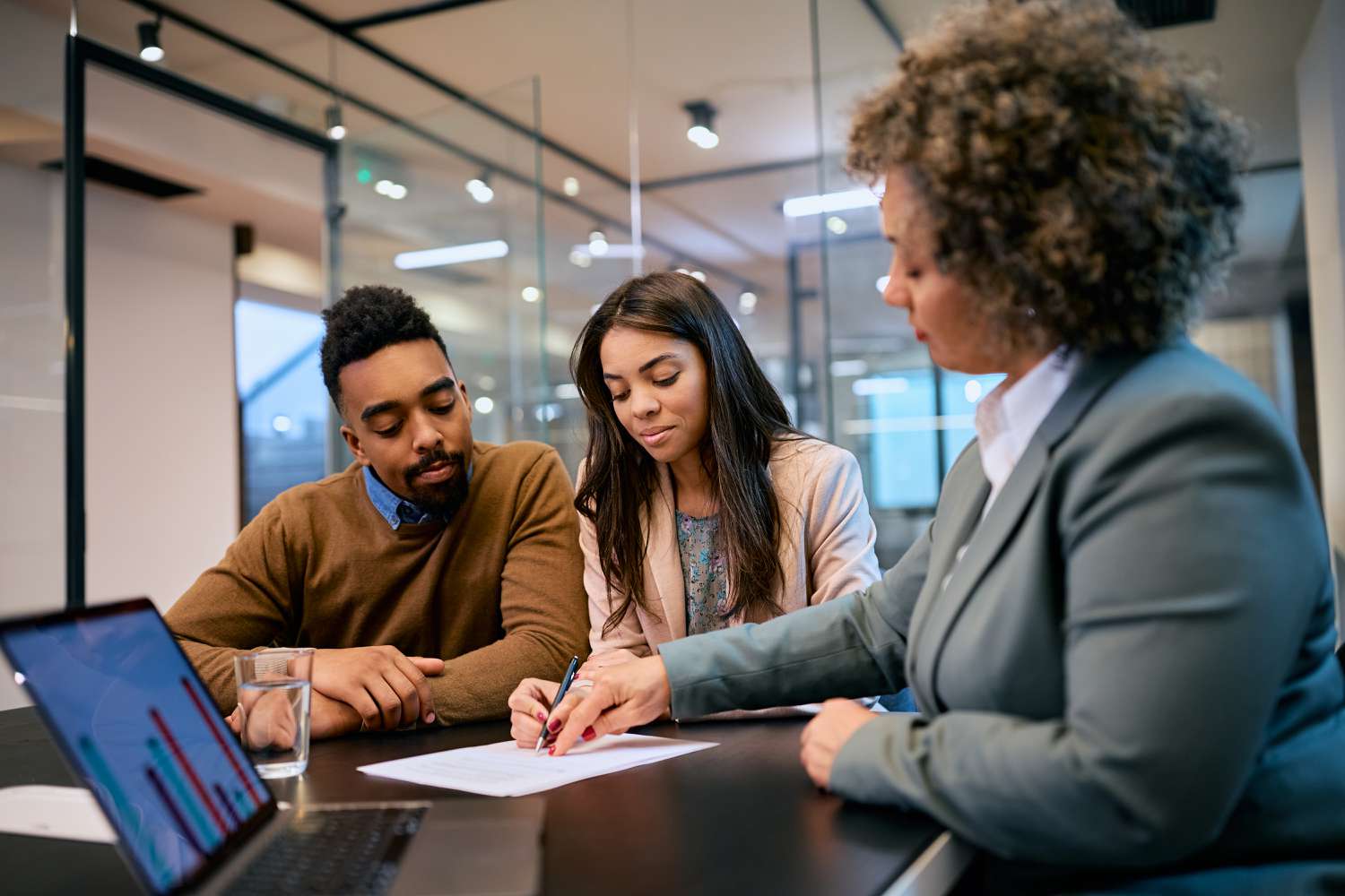 A young couple seated in an office reviews a document as an advisor seated nearby indicates something on the page.