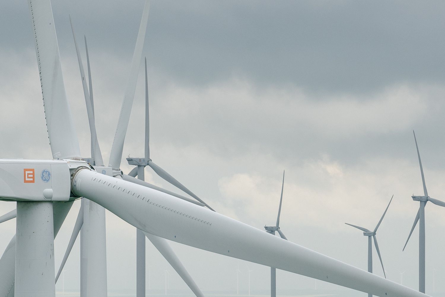 A group of GE Vernova wind turbines are in operation in front of a cloudy sky in Romania.