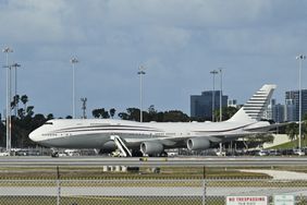 A large passenger jet parked at an airport with stairs extended, cityscape in the background