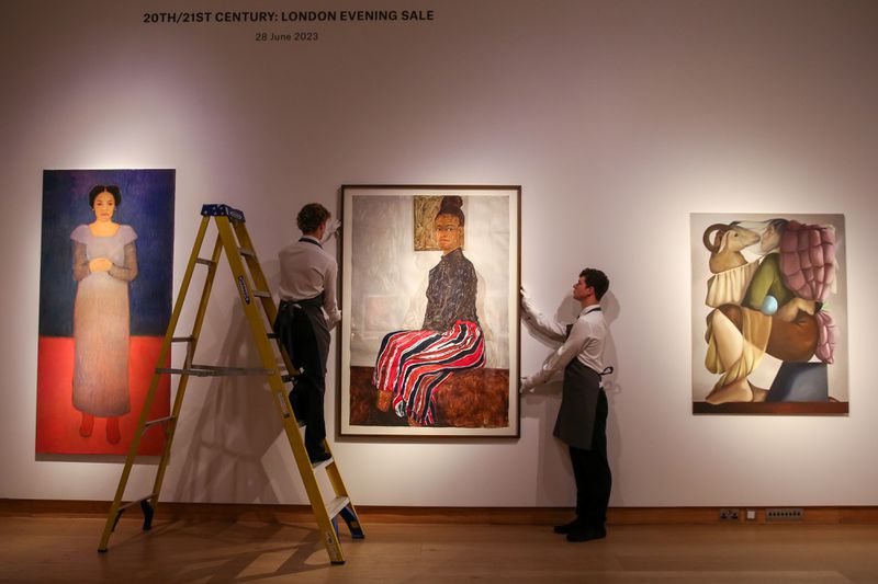 Workers placing art on walls in preparation for an auction