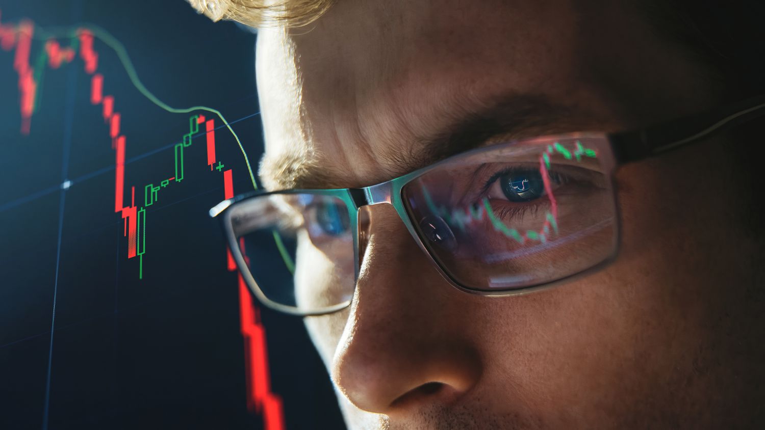 Close-up portrait of focused analyst wearing eyeglasses looking at computer screen analyzing stock market charts.