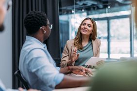 Two colleagues have a discussion at an office table.