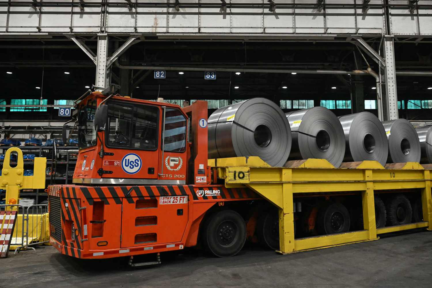 An orange truck is seen with rolls of steel on a trailer behind it.