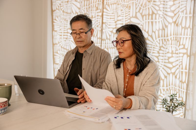 Older couple sitting in their kitchen and looking at mortgage documents and a laptop