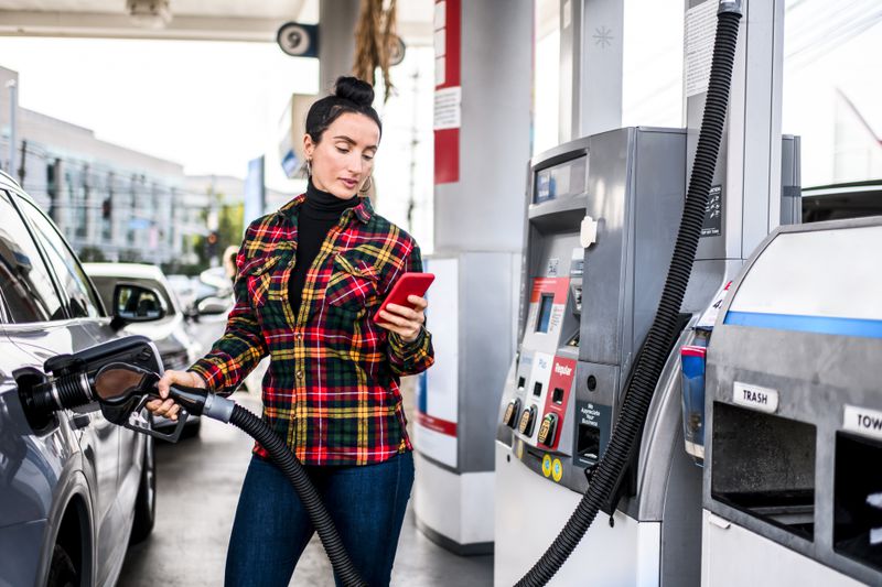 A salesperson looks at phone while pumping gas into a truck on the way to their next client call.