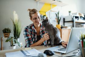 Young woman petting cat while working from home