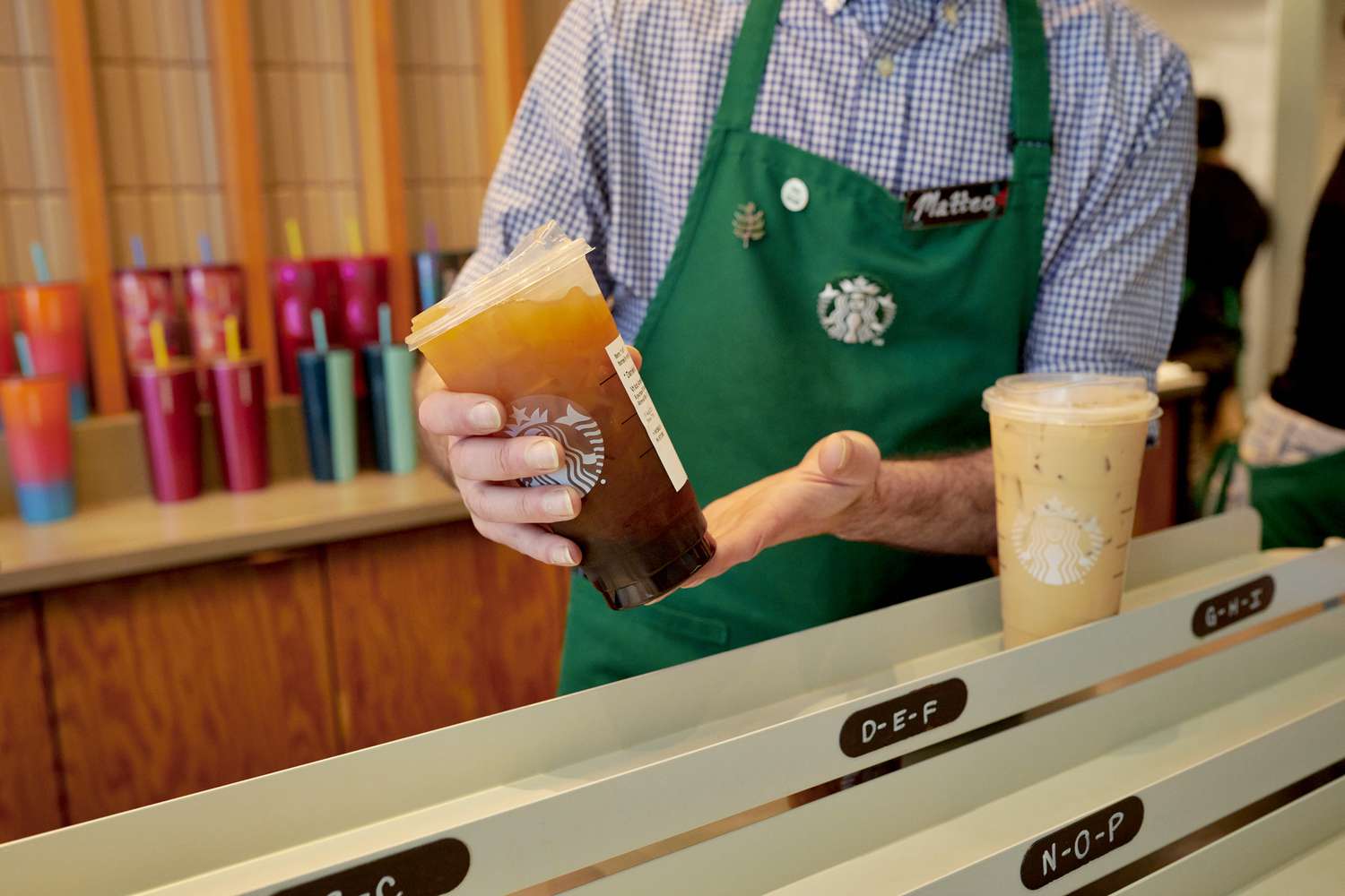 A barista wearing a green Starbucks apron places an iced coffee in the mobile pickup area at a Starbucks location in New York