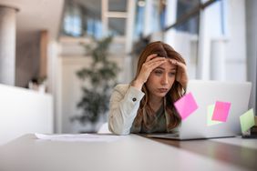 A person at a desk looking at a laptop computer looking anxious.