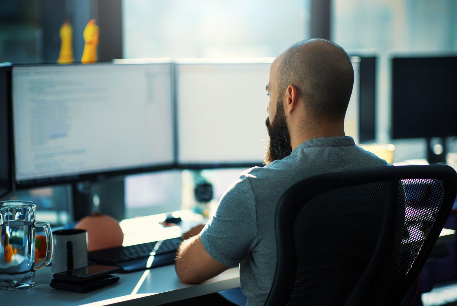 Close-up rear view of a young man coding on multiple computers