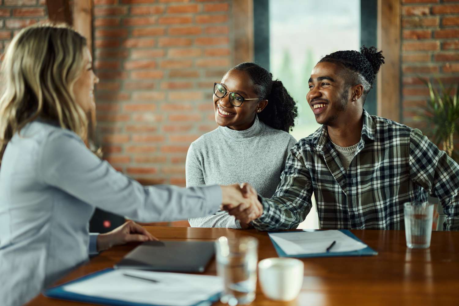 couple shaking real estate agent's hand after signing contract.