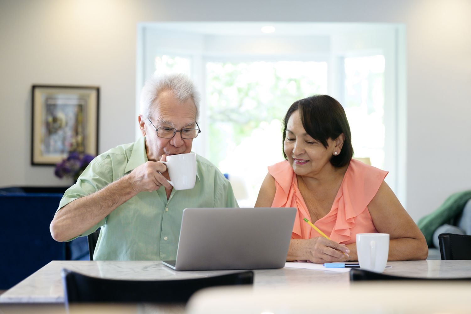 Relaxed senior couple checking interest rates for reverse mortgages on laptop while drinking coffee at home.