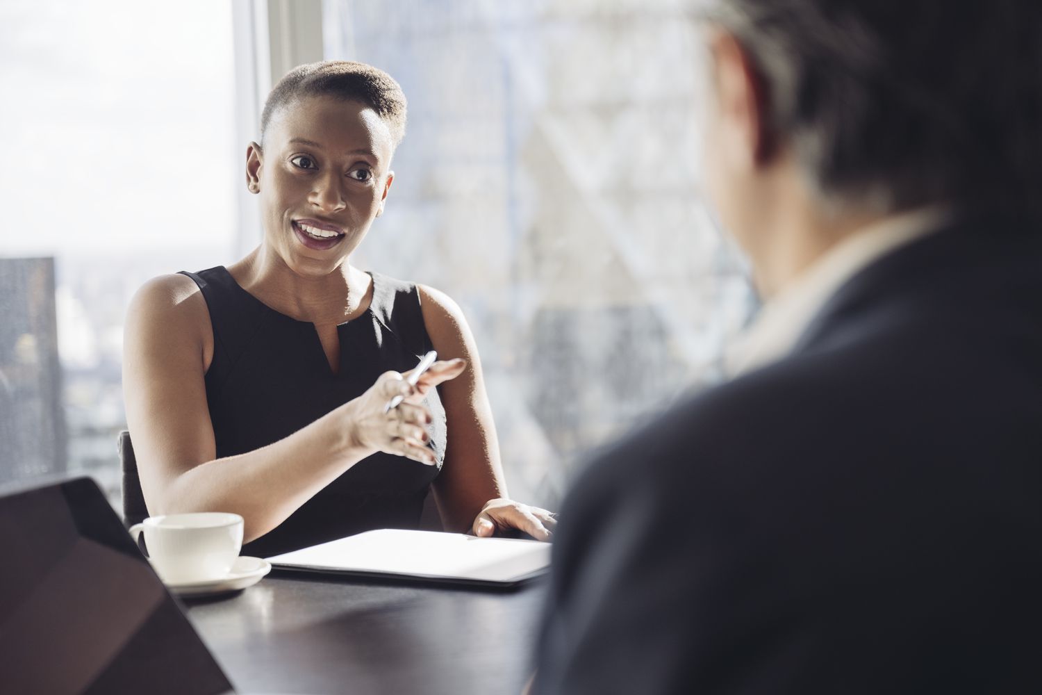 Over the should view of a person in a suit talking to a smiling person focused on them.