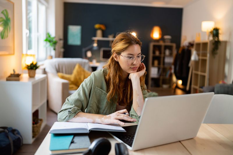 Young woman sitting at home and looking seriously at savings and CD rates on her laptop