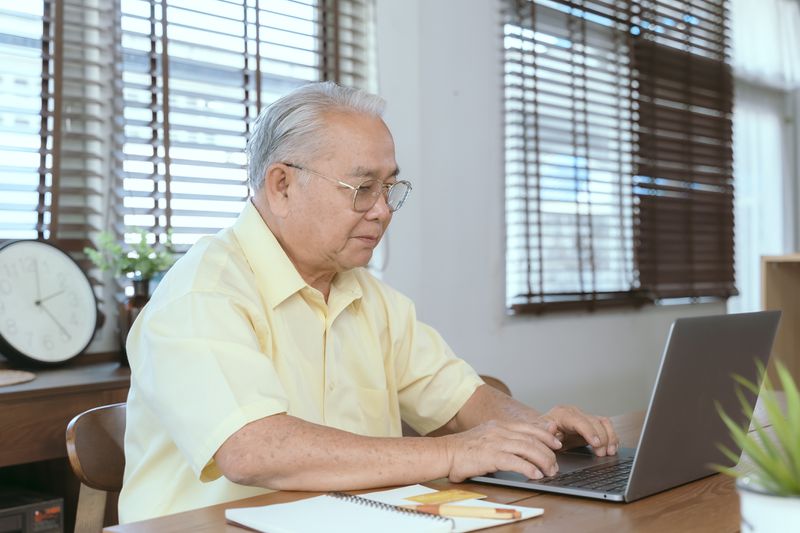 A mature adult investor uses a laptop to determine the date of declared dividends for investments they hold and writes ex-dividend dates into a planning calendar book.