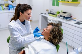 A female dentist looks at a female patient's teeth while she sits in the dentist chair