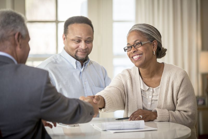 A couple sitting across a desk from their financial advisor and shaking hands