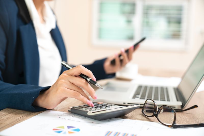 business woman using a calculator and laptop on a table with papers containing graphs and charts