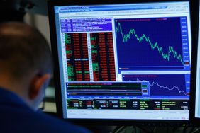 A person looks down while working in front of a computer screen displaying stock data at the New York Stock Exchange