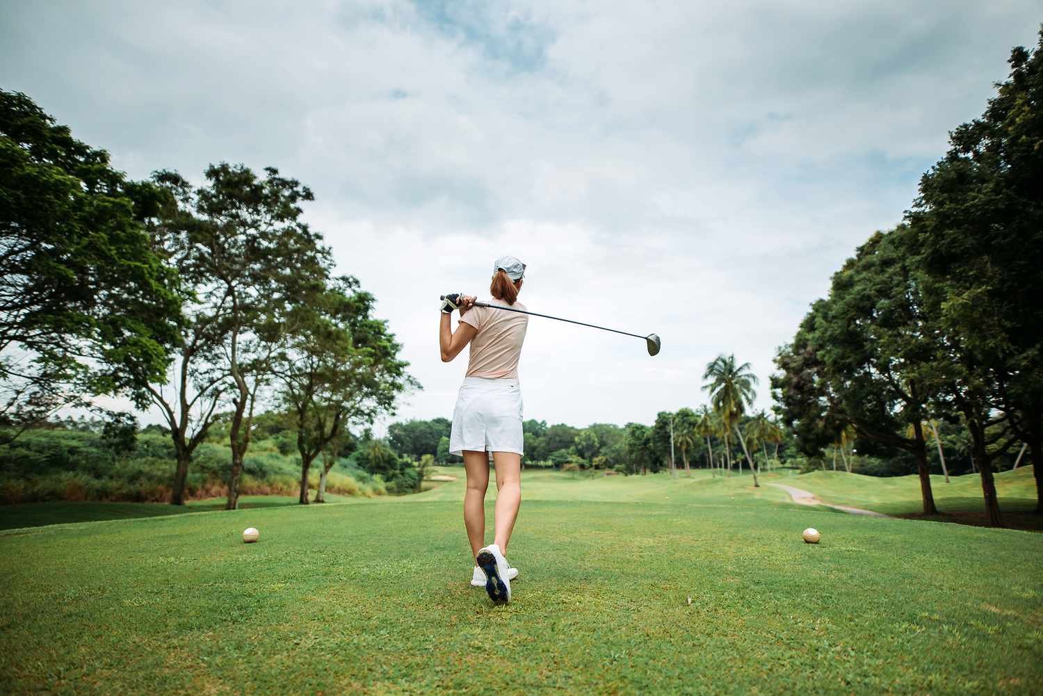 Golfer swinging on a golf course, trees in the background