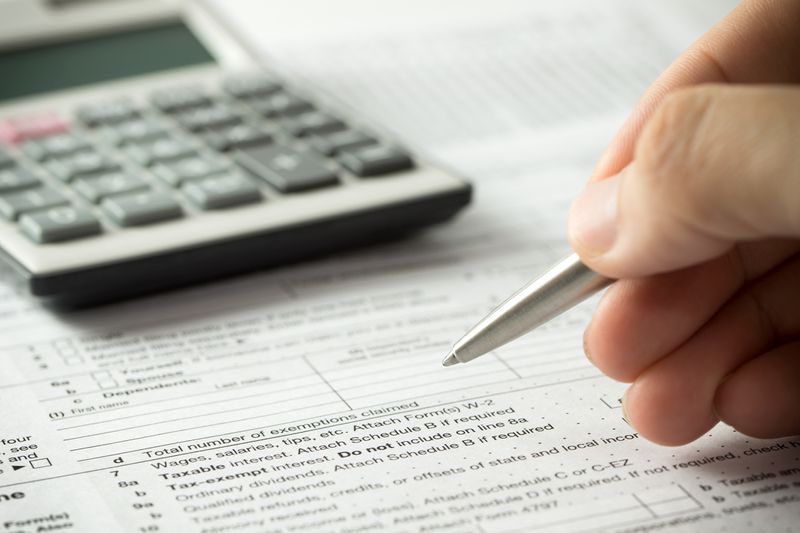 A man filling an income tax return form with pen and calculator.