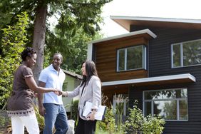 A couple working with a real estate agent, standing outside a house