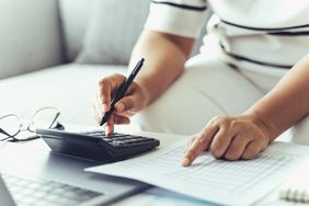 A taxpayer places a finger on the line corresponding to their income tax bracket and enters that percentage into a calculator with the other hand.