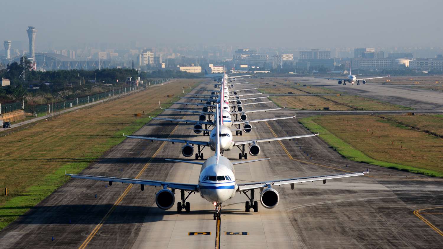 A large number of commercial airplanes on a runway waiting to take off. 