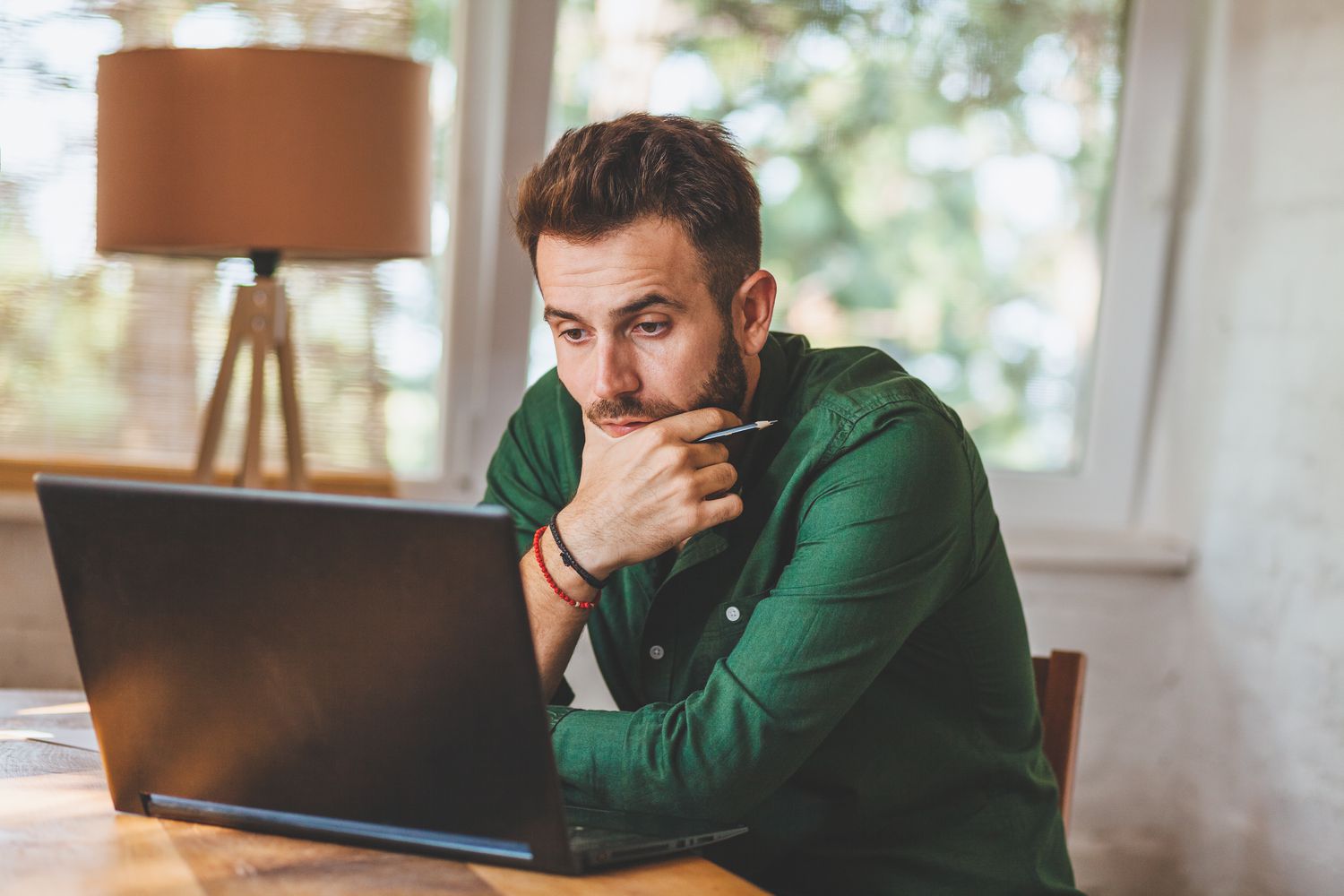 Young man at home, looking intently and with some surprise at his laptop
