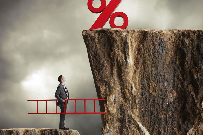 A businessman with a ladder looking up at higher interest rates.