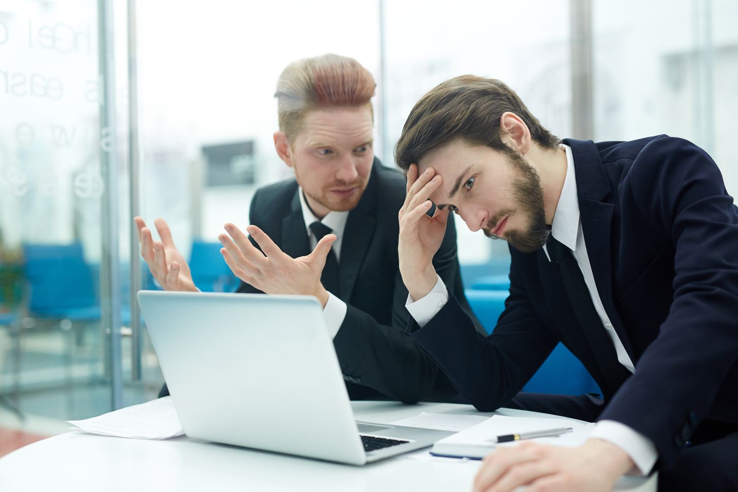 Two bank loan officers look distressed as they review toxic debt numbers on a laptop before an executive meeting.