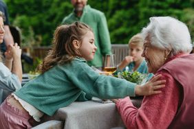 Small child talking to older family member in an outdoor setting at a table.