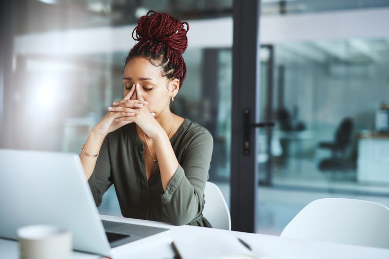 A woman sits at a desk in a thinking pose.