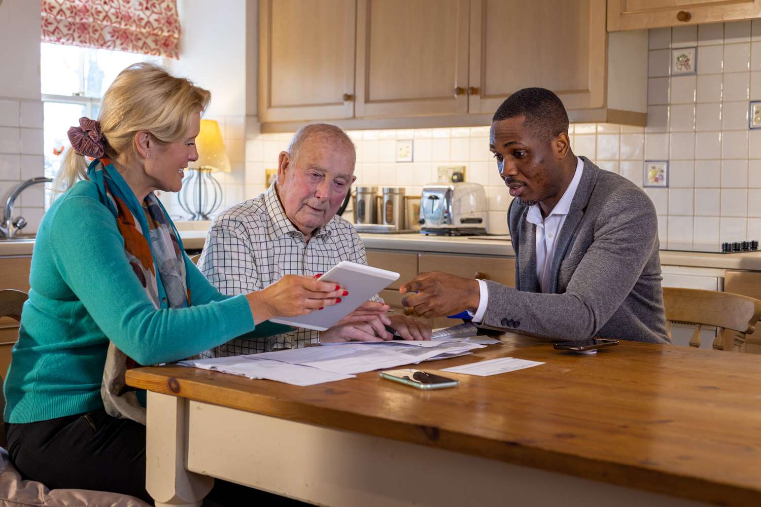 A financial advisor sits at a kitchen table with a senior investor and mature child and explains how they can contribute a gift of funds to an IRA account.