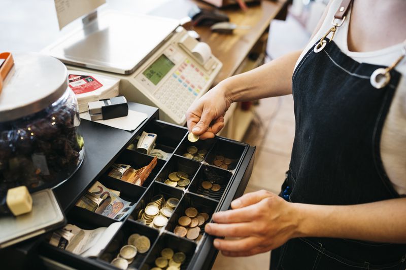 Woman's hand adding some coins to a cash till