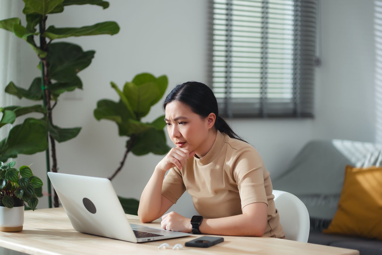 A young woman sitting in her home office, looking concerned as she reviews information on her laptop.