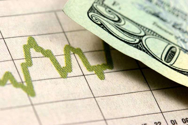 A dollar is overlaid on a newspaper clipping of a graph. 