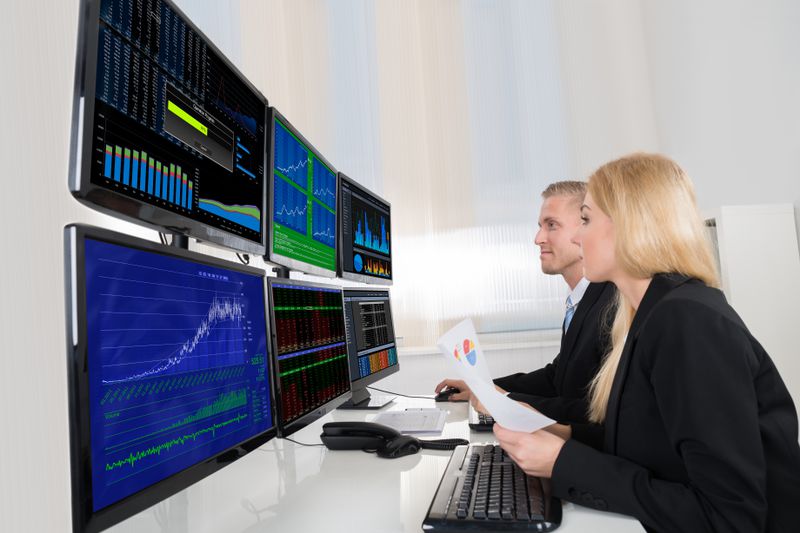 Traders at a desk looking at multiple computer monitors.