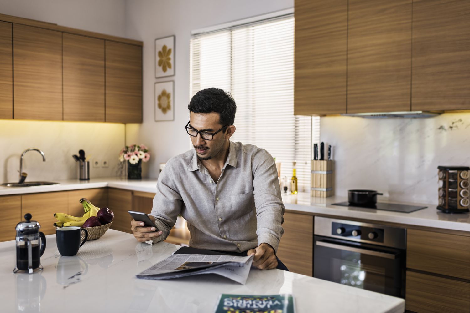Man in a kitchen with a phone and a newspaper