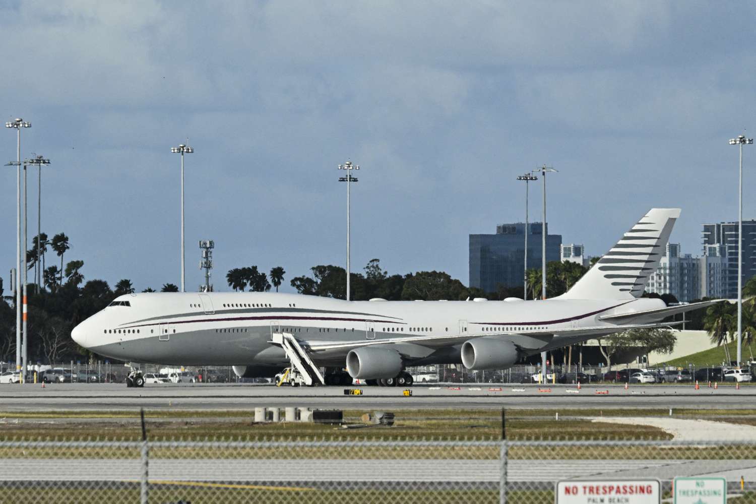A large passenger jet parked at an airport with stairs extended, cityscape in the background