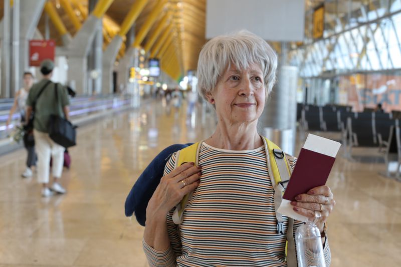 An older traveler holding their passport and tickets holding in an airport terminal.