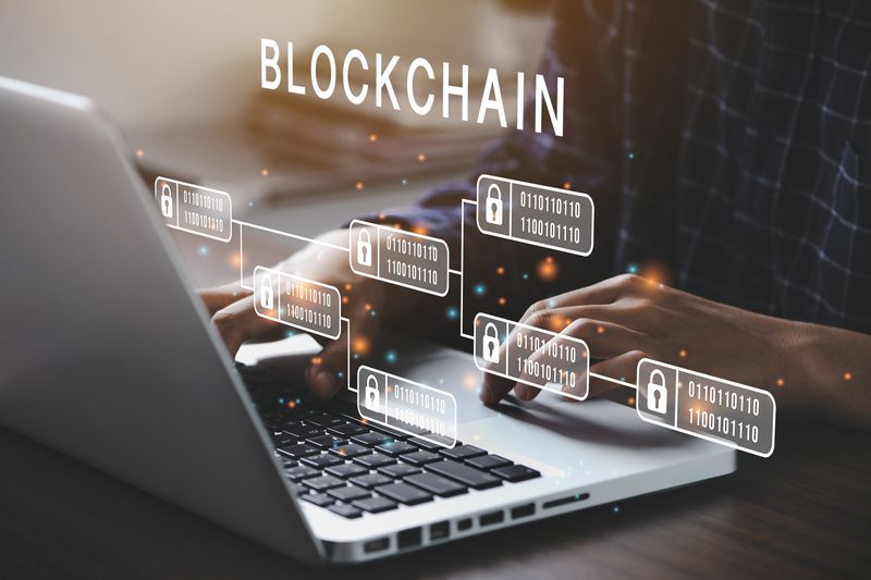 A person typing at a laptop with illustrations of the blockchain floating over the keyboard.