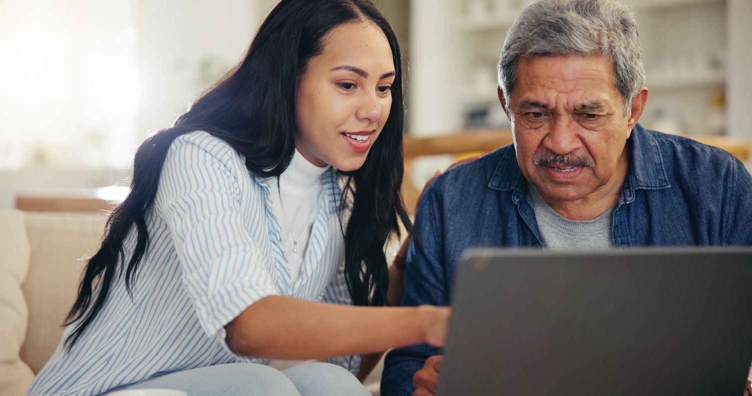 Person with long dark hair and their older parent work on a student financial aid application on a laptop computer.