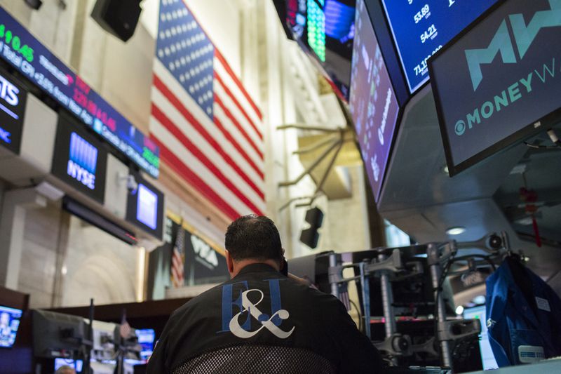 A trader works at a desk on the floor of the New York Stock Exchange, sitting with his back to the camera beneath an American flag.