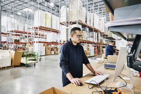 Warehouse worker using a computer inside with a wide shot of the warehouse interior