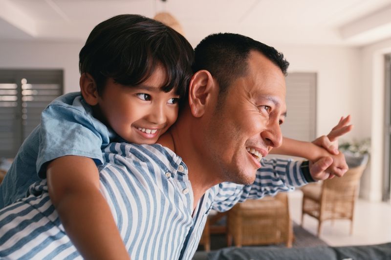 Flying, child and dad with piggyback for playing in home with bonding, fun game and support with smile. Family, man and boy kid on shoulder for airplane fantasy with imagination, trust and freedom