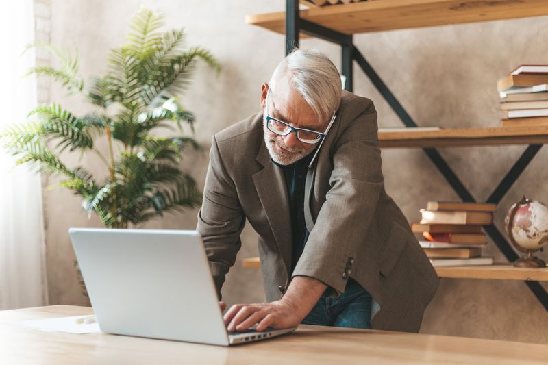 Adult man on laptop, talking on phone in a modern workplace