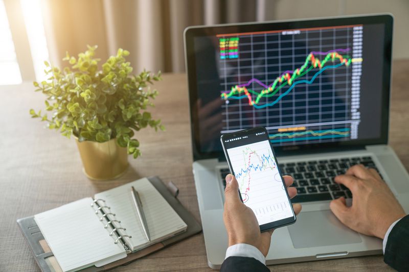 Investor analyzing stock market investments with financial dashboard, business intelligence (BI), and key performance indicators (KPI) on smartphone and computer screens
