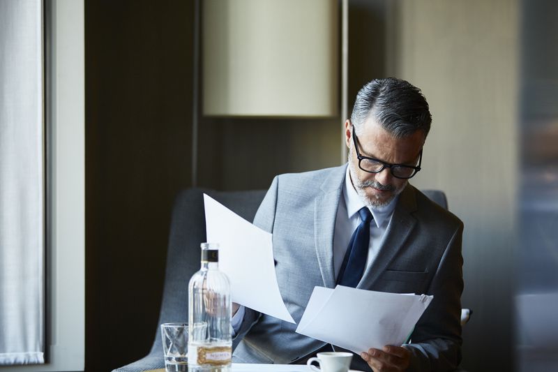 man in a suit looking at papers while at a table with water and espresso in front of him