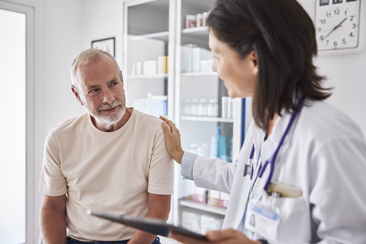 A female doctor comforts a senior male patient in an examination room.