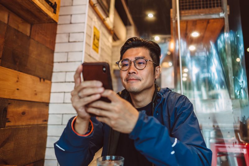 A man sits at a table staring at his smartphone